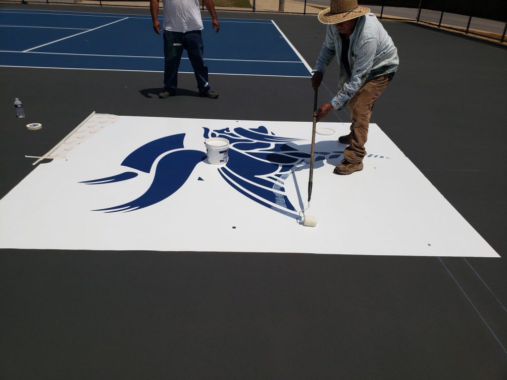 Worker Painting Sports Court Logo with Roller Brush